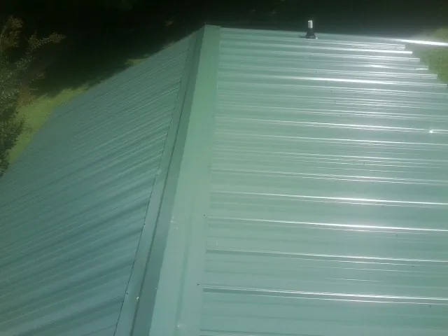 New green metal panels meeting at the ridge of a roof — Flat Roof Repair work by our crew in Chatham