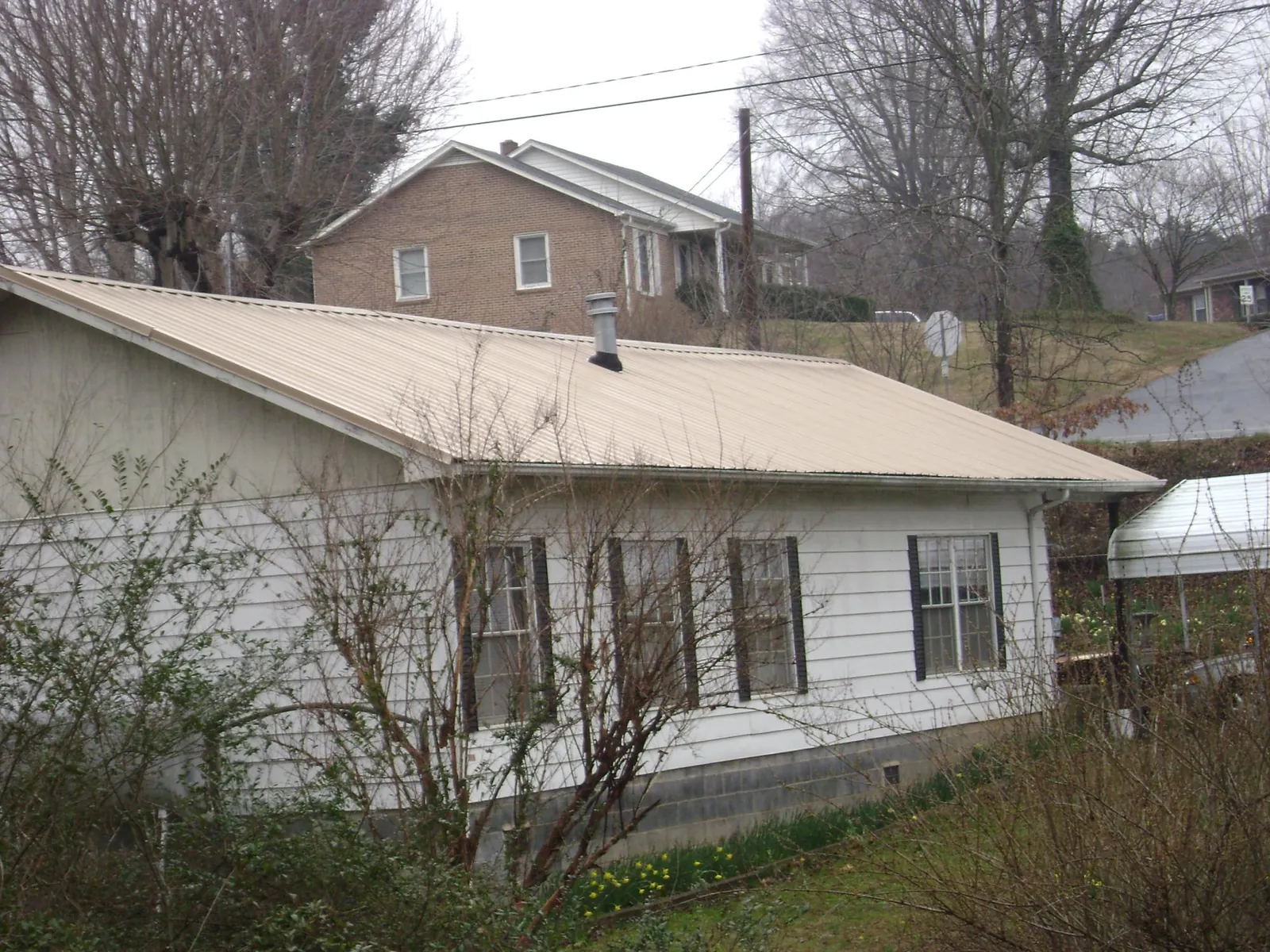 Tan metal roof on a white sided house set into a hillside — Commercial Roofing by Roofing Brothers in Chatham