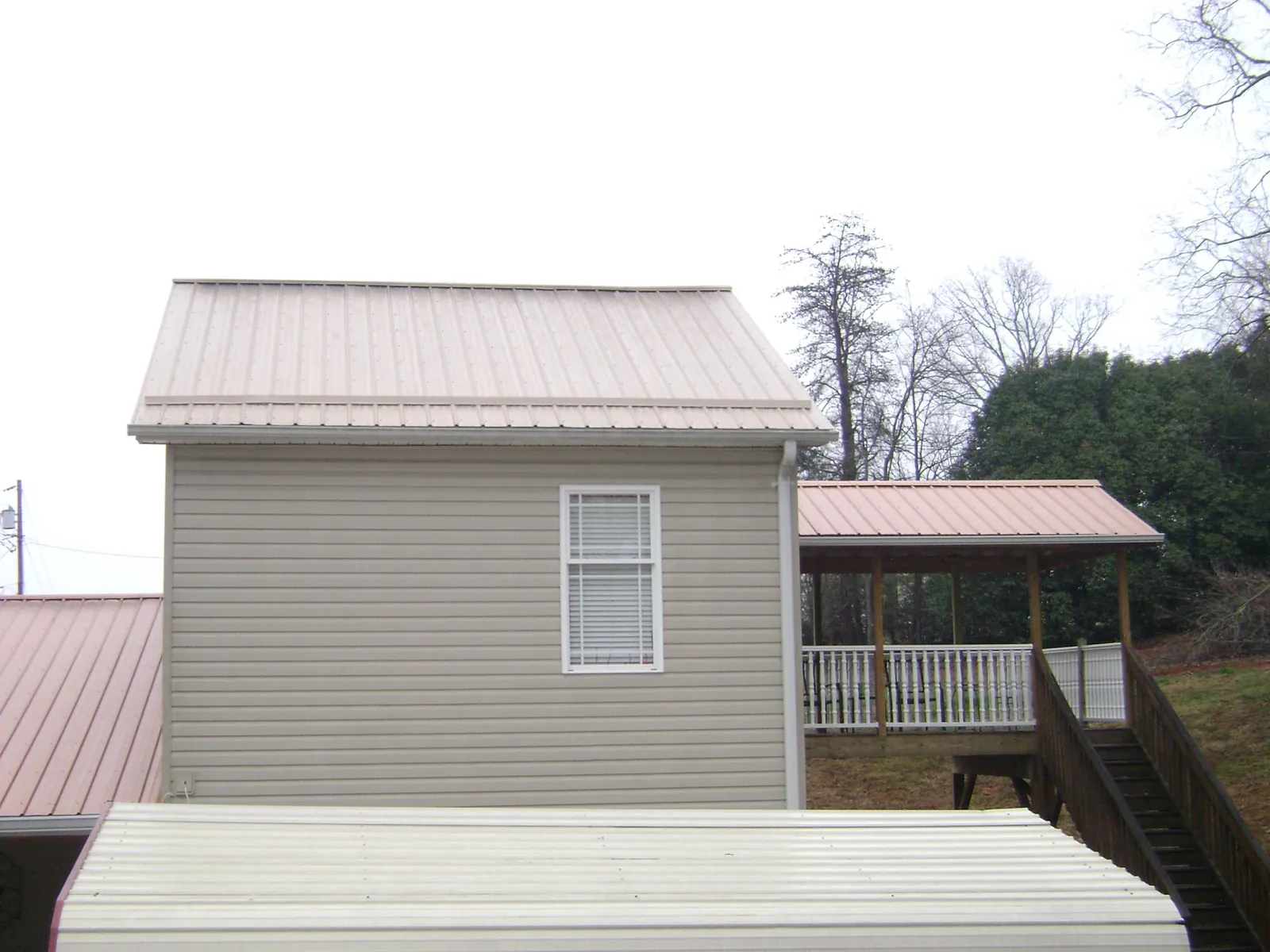 Tan metal roofs on a two story addition and attached porch, from a Roof Replacement job in Chatham